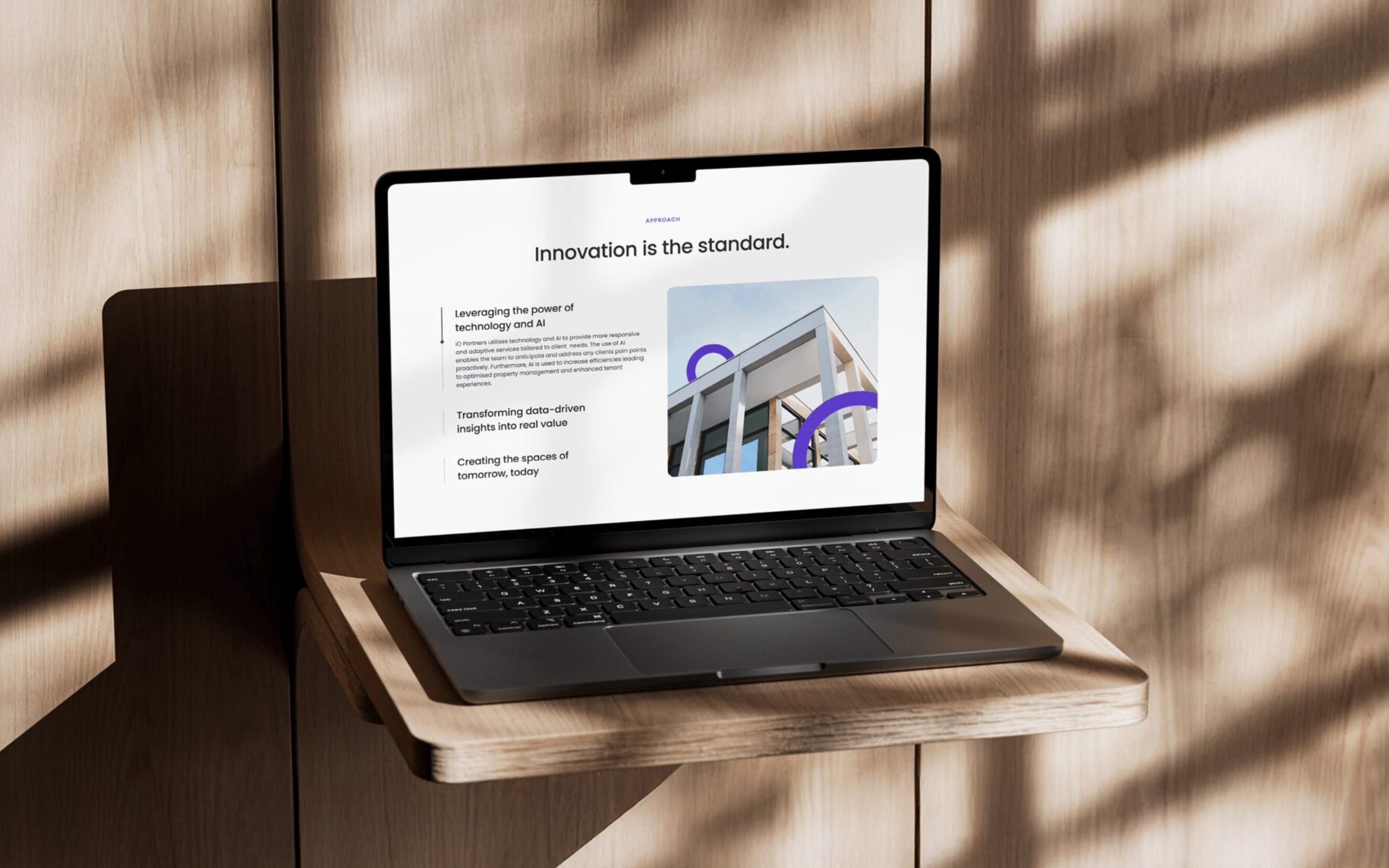 A laptop on a wooden shelf in dappled sunlight, showing the iO Partners page “Innovation is the standard.”