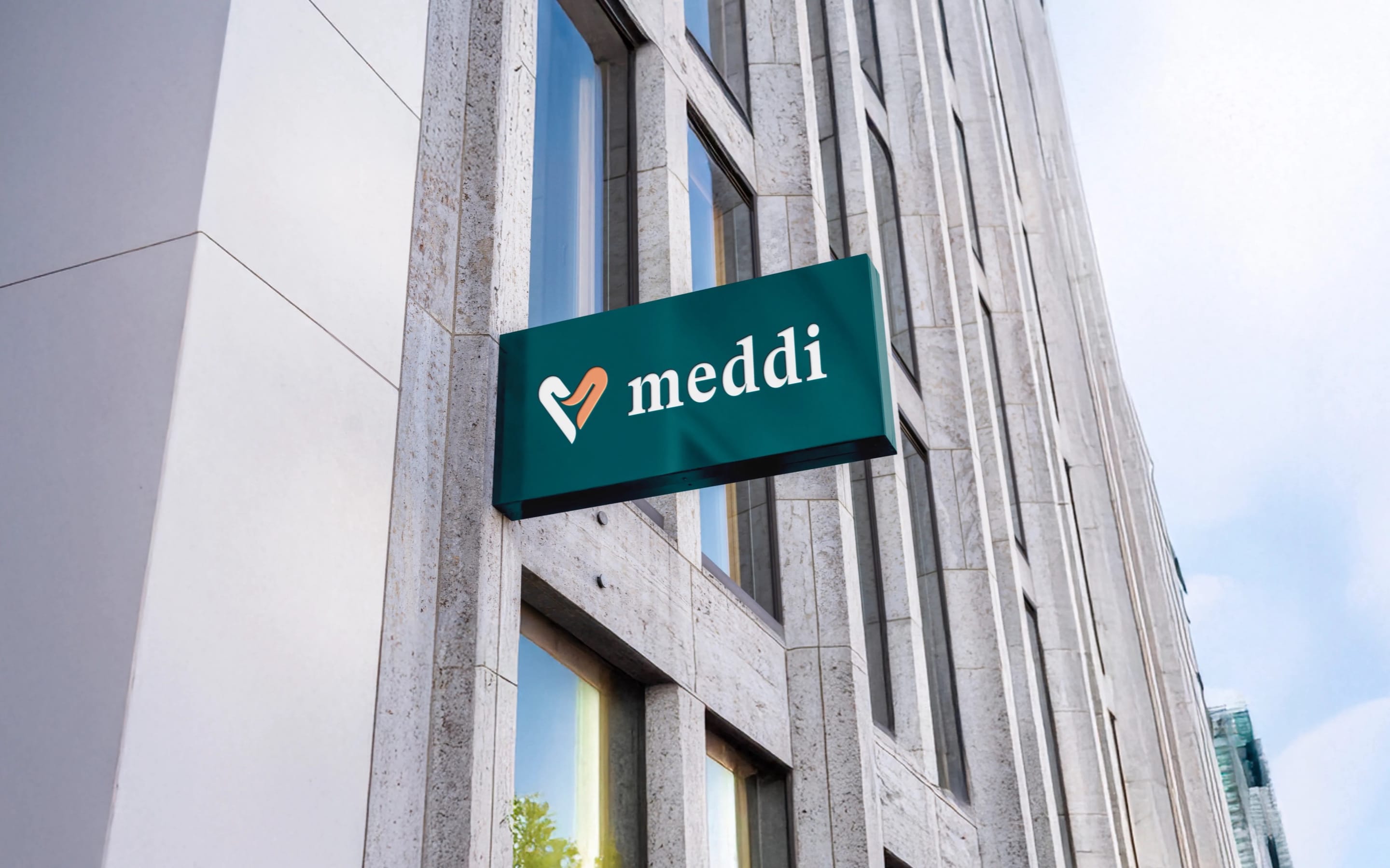 A teal MEDDI sign with the heart-and-hand symbol and serif wordmark on a pale stone office building against a blue sky.