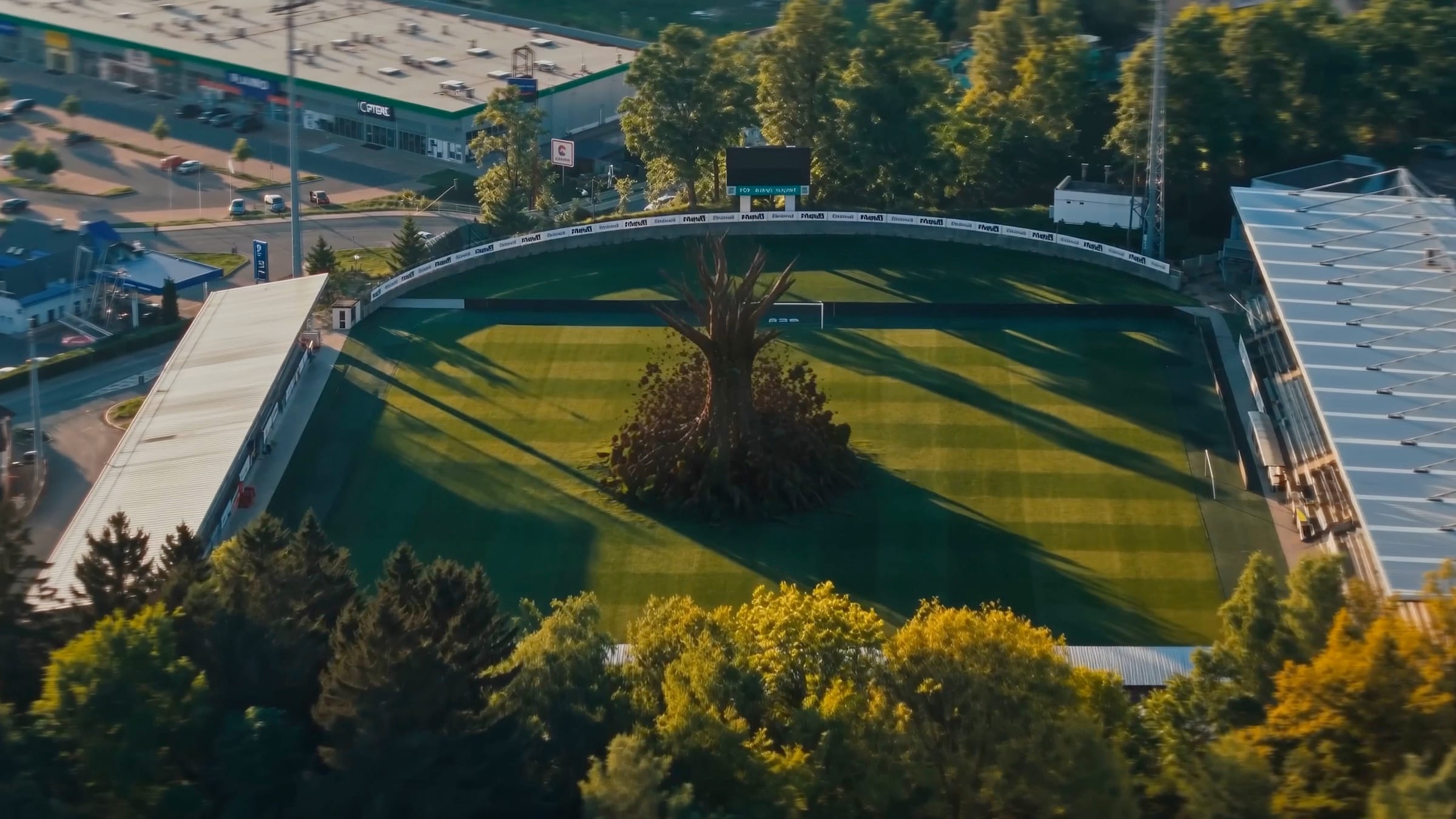 Aerial view of the Jablonec stadium at golden hour, with an apple tree growing from the centre of the pitch.