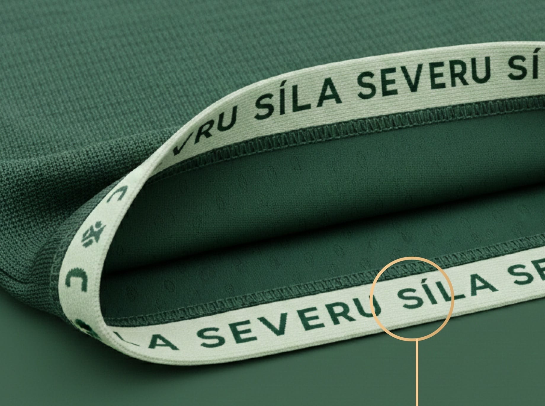 Close-up of a green shirt hem with a pale inner tape reading “SÍLA SEVERU” between tree symbols.