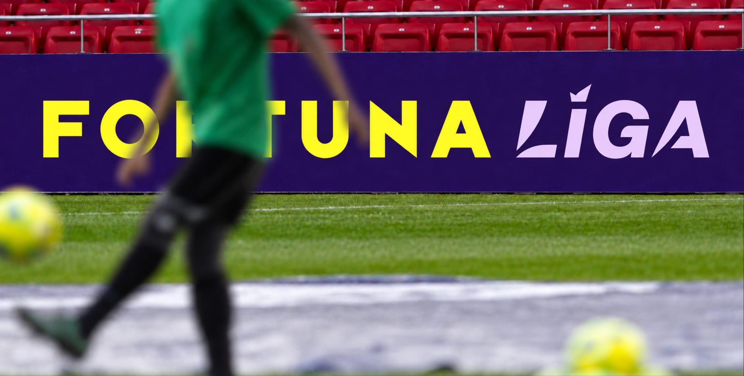 AI-assisted visual: a Fortuna Liga pitchside board in yellow and lilac on purple, a player blurred in the foreground.